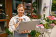 © Yaroslav Astakhov - Beautiful flower shop owner wearing apron working on laptop in her store