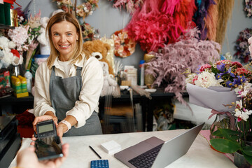 Smiling florist holding POS terminal in floral shop and looking at camera. High quality photo