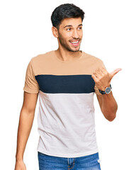 Young handsome man wearing casual clothes smiling with happy face looking and pointing to the side with thumb up.