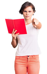 Wall Mural - Beautiful young woman with short hair reading a book pointing with finger to the camera and to you, confident gesture looking serious