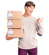 © Krakenimages.com - Young handsome man holding delivery package pointing thumb up to the side smiling happy with open mouth