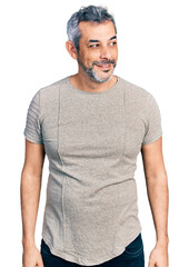 Canvas Print - Middle age hispanic with grey hair wearing casual grey t shirt looking away to side with smile on face, natural expression. laughing confident.