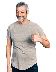 Sticker - Middle age hispanic with grey hair wearing casual grey t shirt doing happy thumbs up gesture with hand. approving expression looking at the camera showing success.