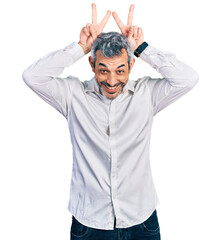 Sticker - Middle age hispanic with grey hair wearing casual white shirt posing funny and crazy with fingers on head as bunny ears, smiling cheerful