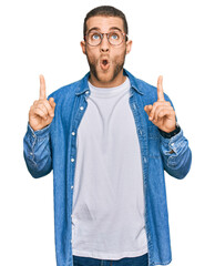 Canvas Print - Young caucasian man wearing casual clothes amazed and surprised looking up and pointing with fingers and raised arms.