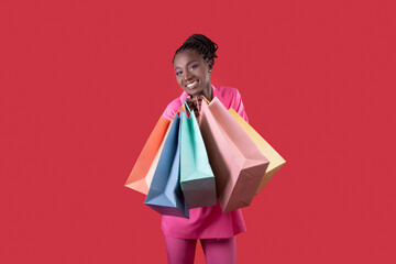 Smiling African Woman With Shopping Bags In Hands Posing Over Red Background