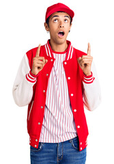 Canvas Print - Young african amercian man wearing baseball uniform amazed and surprised looking up and pointing with fingers and raised arms.