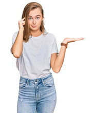 Beautiful Young Blonde Woman Wearing Casual White T Shirt Confused And Annoyed With Open Palm Showing Copy Space And Pointing Finger To Forehead. Think About It.