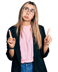 Poster - Hispanic young woman wearing business jacket and glasses pointing up looking sad and upset, indicating direction with fingers, unhappy and depressed.