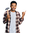 © Krakenimages.com - Young african american man holding hammer smiling happy pointing with hand and finger to the side