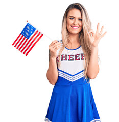 Poster - Young beautiful blonde woman wearing cheerleader uniform holding united states flag doing ok sign with fingers, smiling friendly gesturing excellent symbol