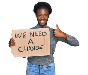 Sticker - Young african american girl holding we need a change banner smiling happy and positive, thumb up doing excellent and approval sign