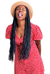 Sticker - Young african american woman wearing summer hat sticking tongue out happy with funny expression. emotion concept.