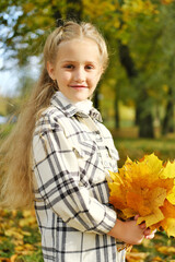 Wall Mural - Little blonde girl posing in a white plaid shirt in an autumn park with a bouquet of yellow leaves