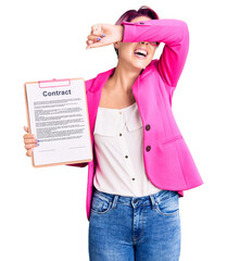 Poster - Young beautiful woman with pink hair holding clipboard with contract document smiling cheerful playing peek a boo with hands showing face. surprised and exited