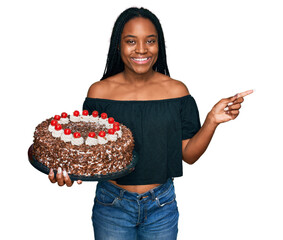 Poster - Young african american woman celebrating birthday holding big chocolate cake smiling happy pointing with hand and finger to the side