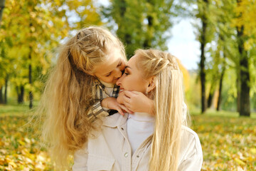 the family has fun in the park. the girl hugs her mother by the neck and kisses her on the nose