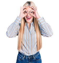 Wall Mural - Beautiful blonde woman wearing casual striped shirt doing ok gesture like binoculars sticking tongue out, eyes looking through fingers. crazy expression.