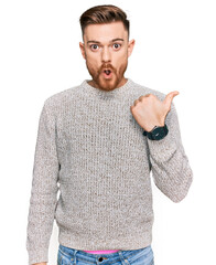 Young redhead man wearing casual winter sweater surprised pointing with hand finger to the side, open mouth amazed expression.