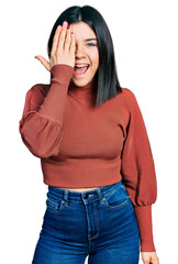 Poster - Young brunette woman with blue eyes wearing elegant sweater covering one eye with hand, confident smile on face and surprise emotion.