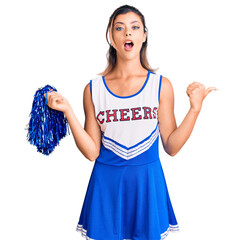 Canvas Print - Young beautiful woman wearing cheerleader uniform surprised pointing with hand finger to the side, open mouth amazed expression.