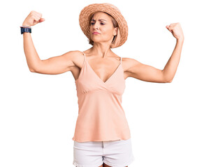 Canvas Print - Young blonde woman wearing summer hat showing arms muscles smiling proud. fitness concept.