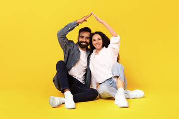 Wall Mural - Eastern Couple Making Roof Joining Hands Sitting Over Yellow Background