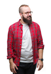 Poster - Young caucasian hipster man wearing glasses over isolated background looking away to side with smile on face, natural expression. Laughing confident.