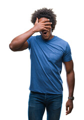 Poster - Afro american man over isolated background peeking in shock covering face and eyes with hand, looking through fingers with embarrassed expression.