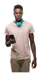 Poster - Young african american man wearing headphones and holding smartphone with a confident expression on smart face thinking serious