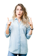 Beautiful young blonde woman over isolated background amazed and surprised looking up and pointing with fingers and raised arms.