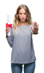 Poster - Beautiful young blonde woman holding degree certificate over isolated background with open hand doing stop sign with serious and confident expression, defense gesture