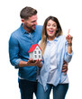 © Krakenimages.com - Young couple in love holding house over isolated background surprised with an idea or question pointing finger with happy face, number one