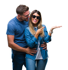 Wall Mural - Young couple in love wearing sunglasses over isolated background amazed and smiling to the camera while presenting with hand and pointing with finger.