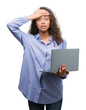 © Krakenimages.com - Young hispanic woman holding computer laptop stressed with hand on head, shocked with shame and surprise face, angry and frustrated. Fear and upset for mistake.