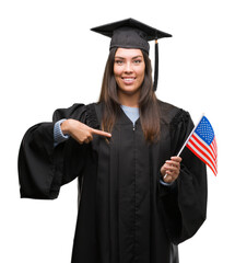 Poster - Young hispanic woman wearing graduated uniform holding flag of america with surprise face pointing finger to himself