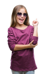 Wall Mural - Young beautiful girl wearing sunglasses over isolated background with a big smile on face, pointing with hand and finger to the side looking at the camera.