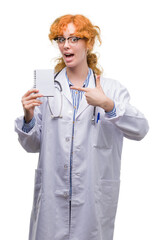 Poster - Young redhead doctor woman holding blank notebook very happy pointing with hand and finger