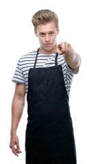 Sticker - Young handsome blond man wearing apron pointing with finger to the camera and to you, hand sign, positive and confident gesture from the front