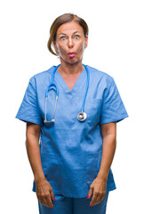 Sticker - Middle age senior nurse doctor woman over isolated background making fish face with lips, crazy and comical gesture. Funny expression.