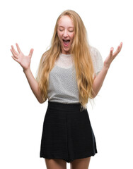 Sticker - Blonde teenager woman wearing moles shirt celebrating mad and crazy for success with arms raised and closed eyes screaming excited. Winner concept