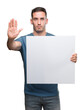 © Krakenimages.com - Handsome young man holding advertising banner with open hand doing stop sign with serious and confident expression, defense gesture