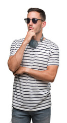 Wall Mural - Handsome young man wearing headphones looking confident at the camera with smile with crossed arms and hand raised on chin. Thinking positive.