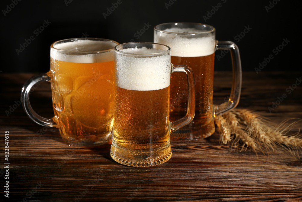 Mugs of cold beer and spikelets on wooden table