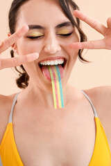 Sticker - Young woman in swimsuit eating jelly candy on beige background, closeup