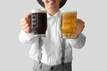 Young man in traditional German clothes with beer on light background, closeup