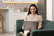 © New Africa - Happy woman working with laptop on sofa in kitchen