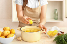 Woman Putting Peeled Potato In Pot At Table In Kitchen