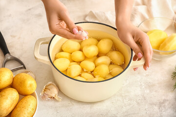 Woman adding salt into pot with peeled potatoes on light background