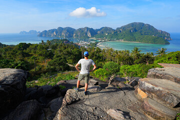 Man standing on a rock on top of a mountain offering a view over Koh Phi Phi Don island in the Andaman Sea at Viewpoint 2 in the Province of Krabi, Thailand